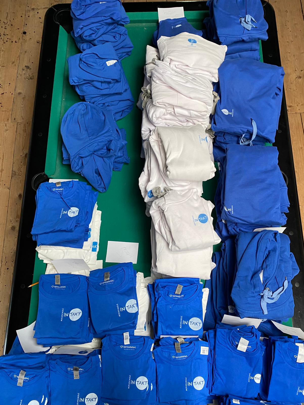 Die INTAKT Shirts und Hoodies liegen auf unserem Billardtisch verteilt